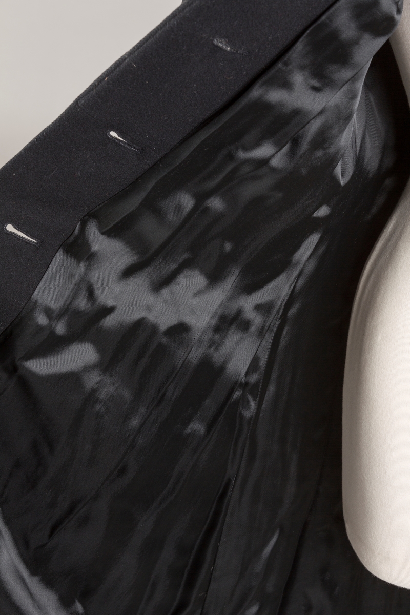 Innsvinget liv, pynteklaffer ved brystet foran. 
Stikklommer foran.
Skulderputer
Fire trukne knapper
Avrundet krage