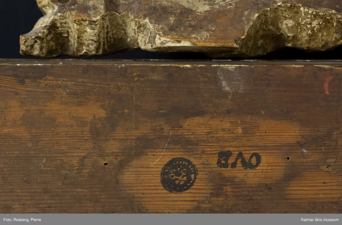 KLM 45592. Spegel, väggspegel. Utförd i sengustaviansk stil. Skuren ornamentik i trä och i gjutet pastellage, förgylld med slagmetall. Ovanför glaset en rund medaljong med relief. Fasetterat originalglas. Träskuret krön i form av en avtagbar rosett.