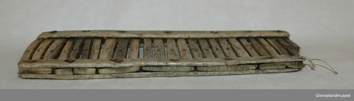 Sammensatt av 3-5 spiler i hver del. Ett hull i de fleste spilene. Den nest ytterste spilen på den ene siden har to hull, og den ytterste på samme side er brukket av.. Tilsammen 25 spiler. Delene er festet sammen med metallnagler.
Ingen dekor.