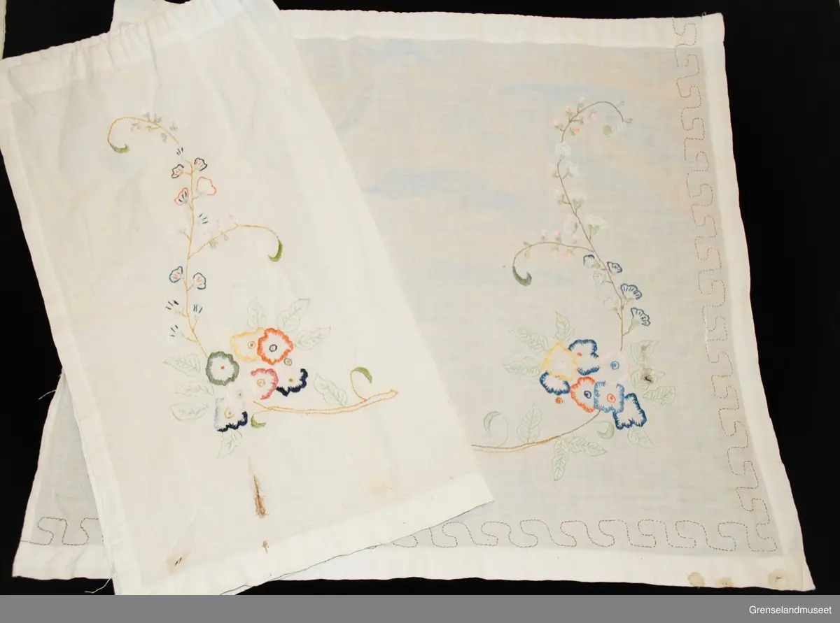 gardinene består av to små fag for nederdelen av stuevindu. Brodert med blomstermotiv i tungesting, kontursting og sjattersøm. Rundt gardinen er en z-kant sydd med sparesting. Løpegang for gardinwire.