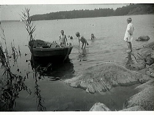 Barnlek. Badande barn vid eka. En pojke står i särk på stenarna vid vattnet. Förlaga till målning.