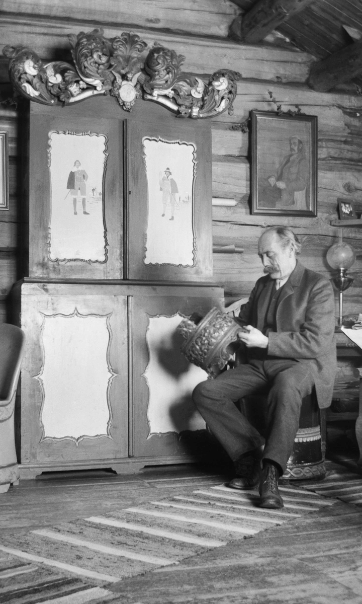 Ivar Kleiven sitter forran et utskjert skap med dekor og en grautambar som han holder i hendene.