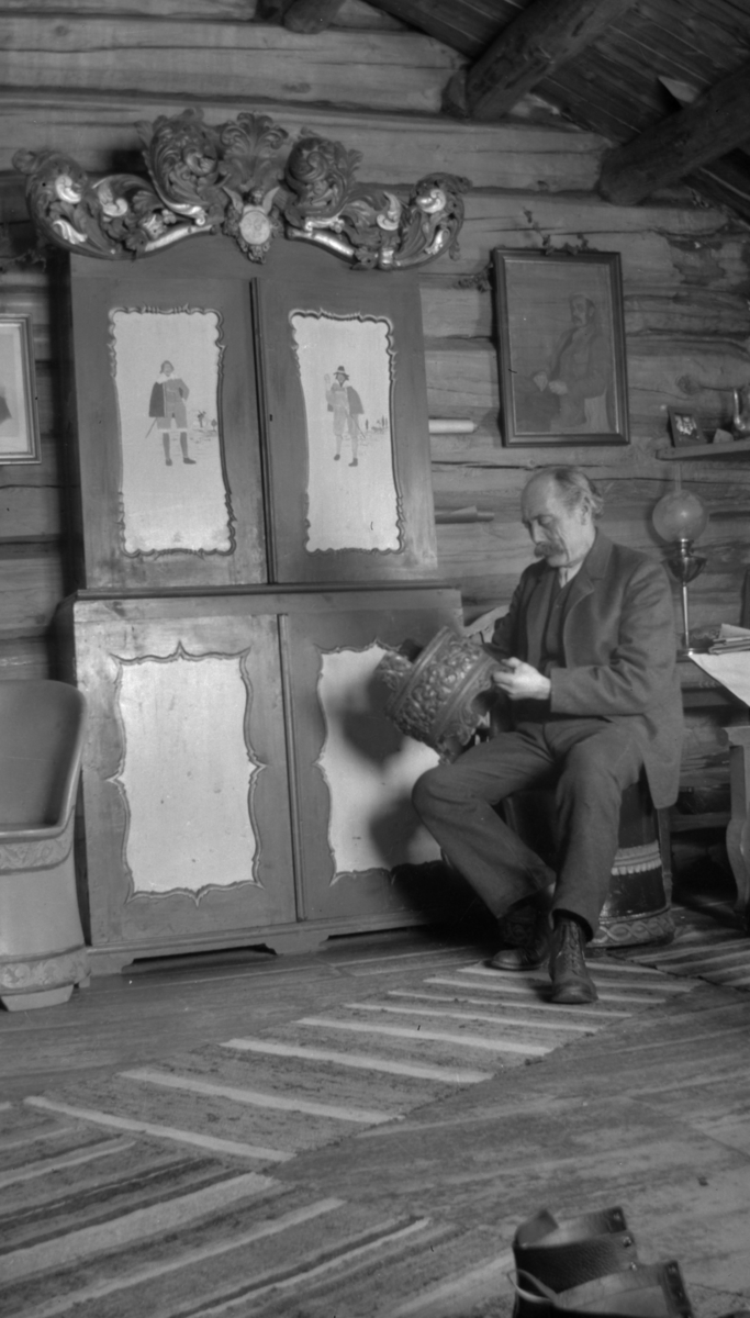 Ivar Kleiven sitter forran et utskjert skap med dekor og en grautambar som han holder i hendene.