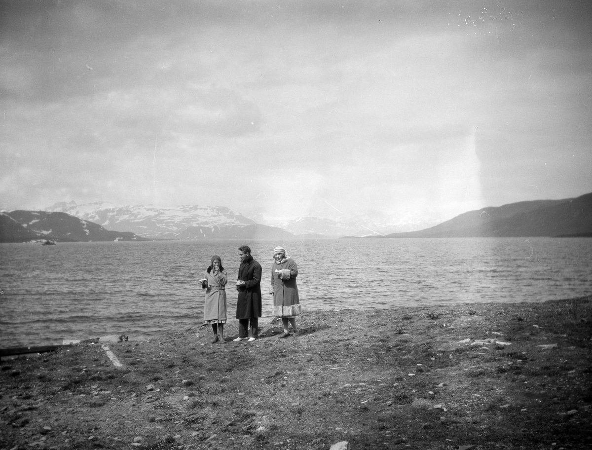 Stort fjellvann med tre mennesker i forgrunn. Muligens ved Tyin.