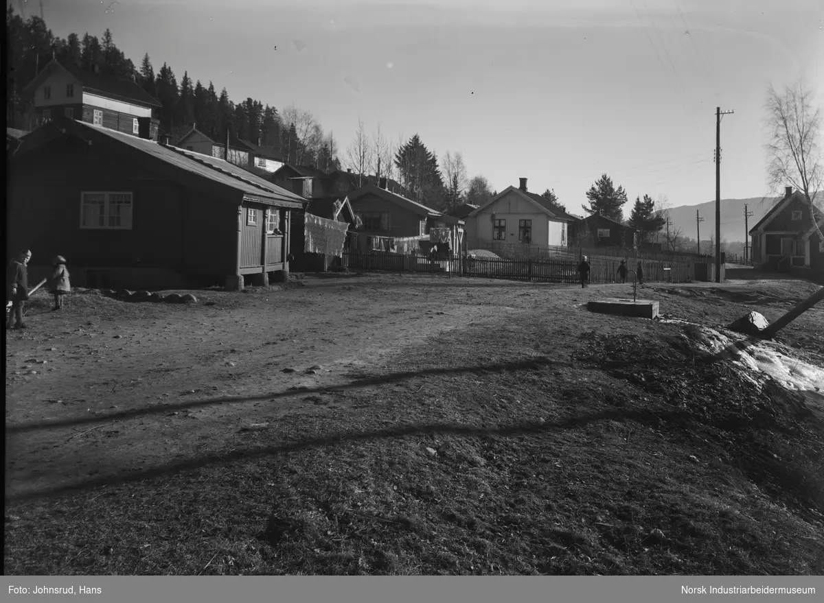 Barn leker i gaten ved boligområde Hyttebyen (Kanalbyen). Klær henger til tørk utenfor flere hus.