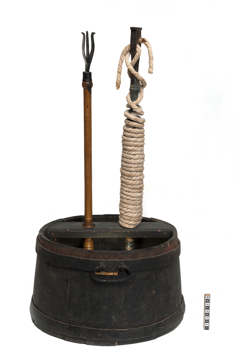 Luntbalja av trä med två järnband och två handtag av järn. Över baljan finns tvärslå med två hål för luntstakar. I botten under slån förstärkning med fördjupning för laddstakarnas ändar.