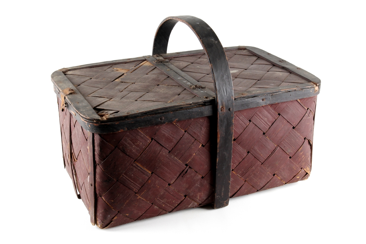 Brunmalt korg flettet av spon. En stor rund hank på midten og to lokk. Bare det ene kan åpnes.