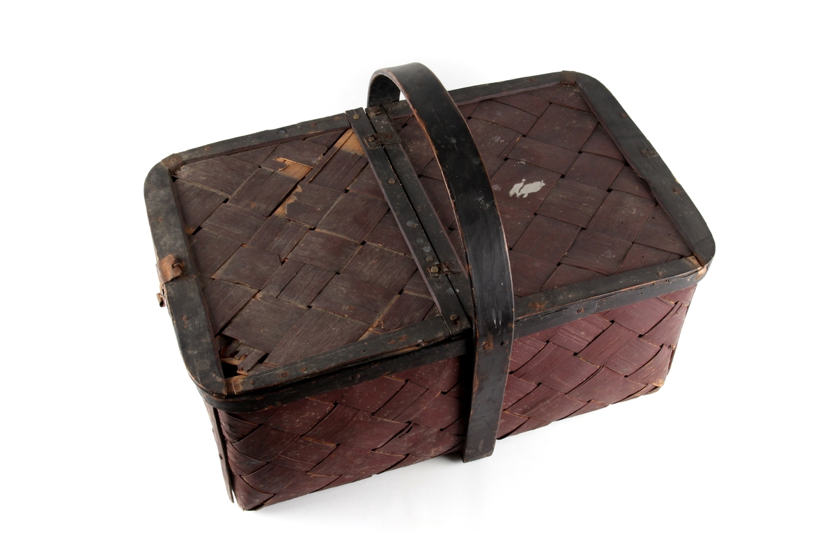 Brunmalt korg flettet av spon. En stor rund hank på midten og to lokk. Bare det ene kan åpnes.