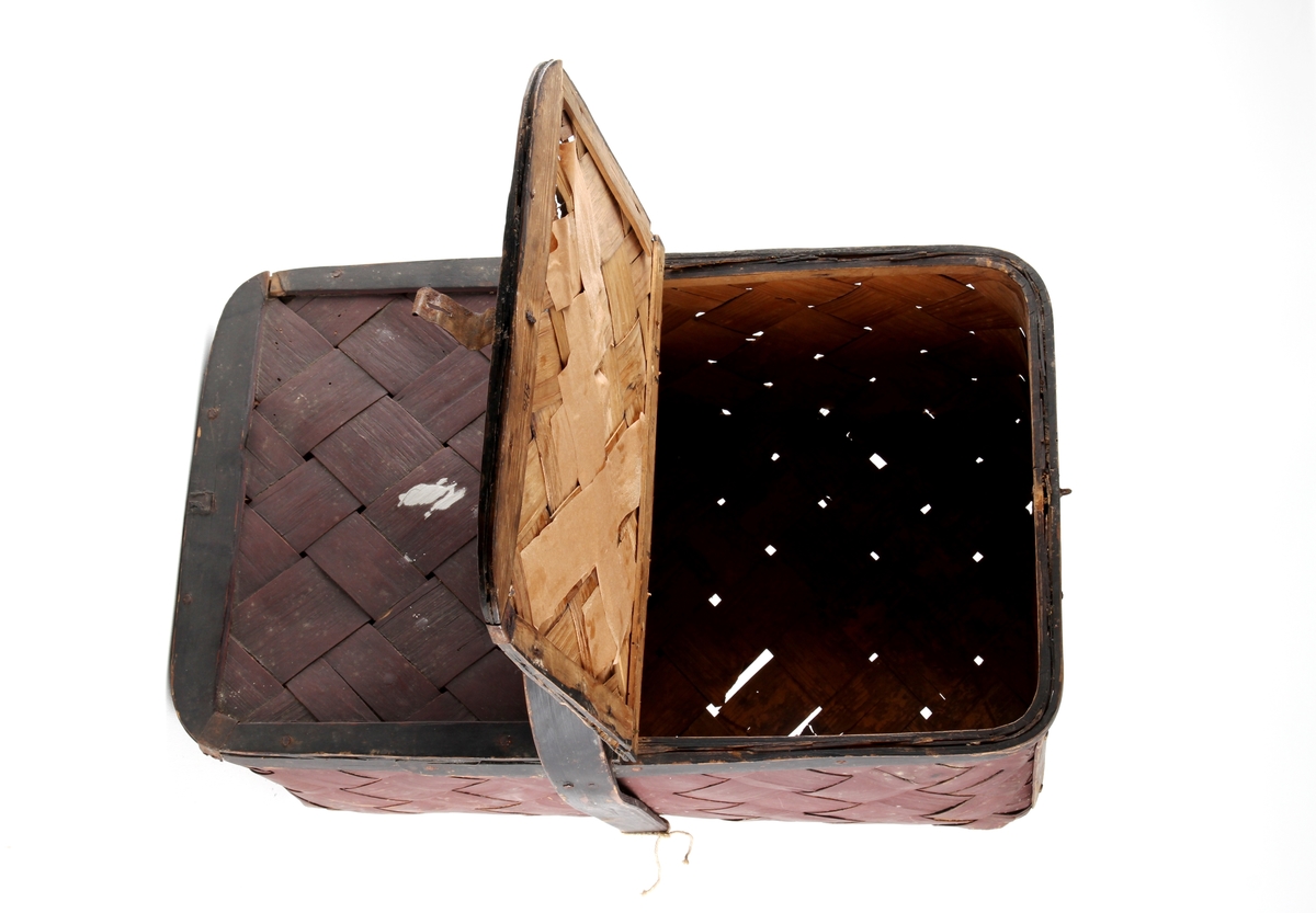 Brunmalt korg flettet av spon. En stor rund hank på midten og to lokk. Bare det ene kan åpnes.