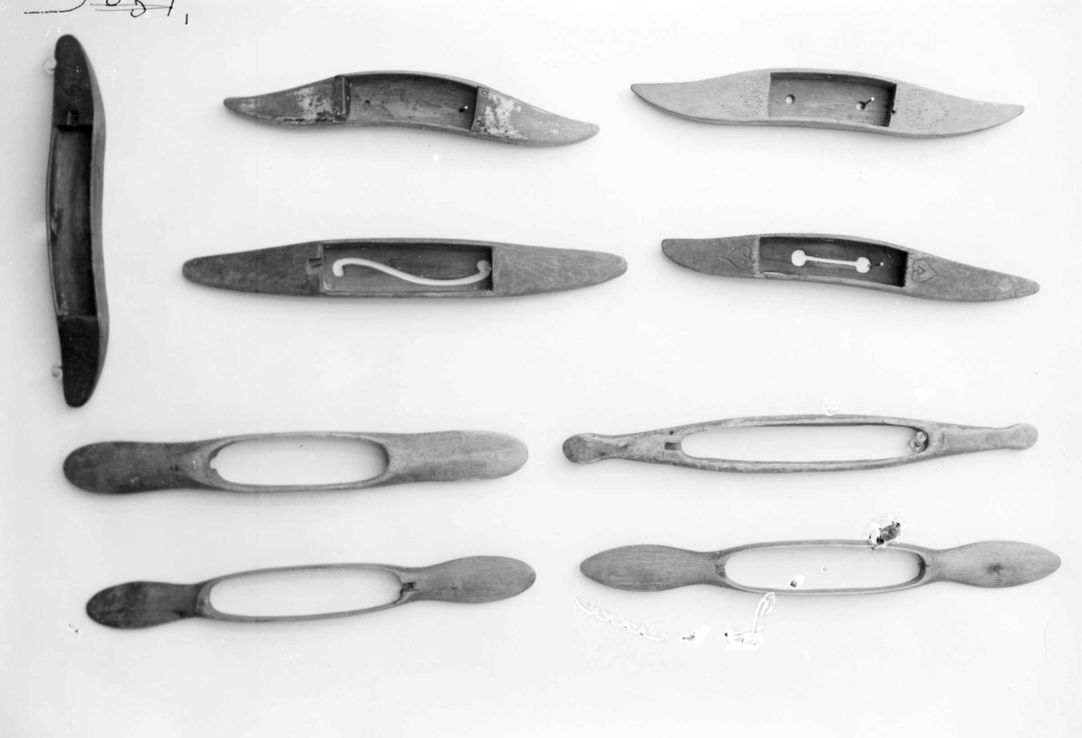 Avlang vevskyttel med flate håndtak i hver ende. Det er skåret ut et hull på midten med spile som det er surret et papir rundt.