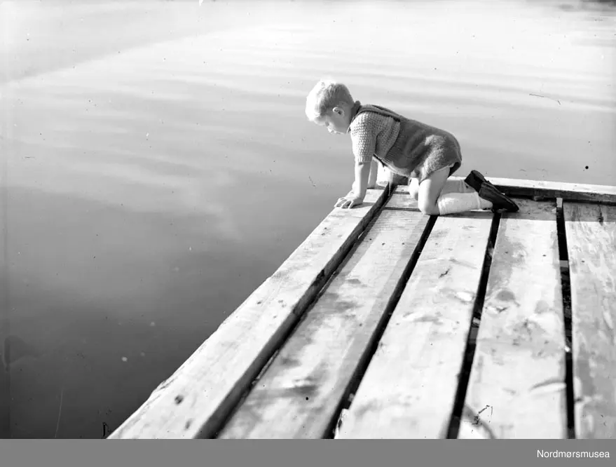 Fisktrappa i Kristiansund har vært møtested for sjøfarende og byens folk i flere generasjoner. Her fra 1930-tallet. Foto: John Myren. Film Noir-estetikk, siluett.  fiskere med sine fartøy, ved fisketrappa på Kirkelandet i Kristiansund. merk kranene langs havna. Fra Nordmøre museums fotosamlinger.