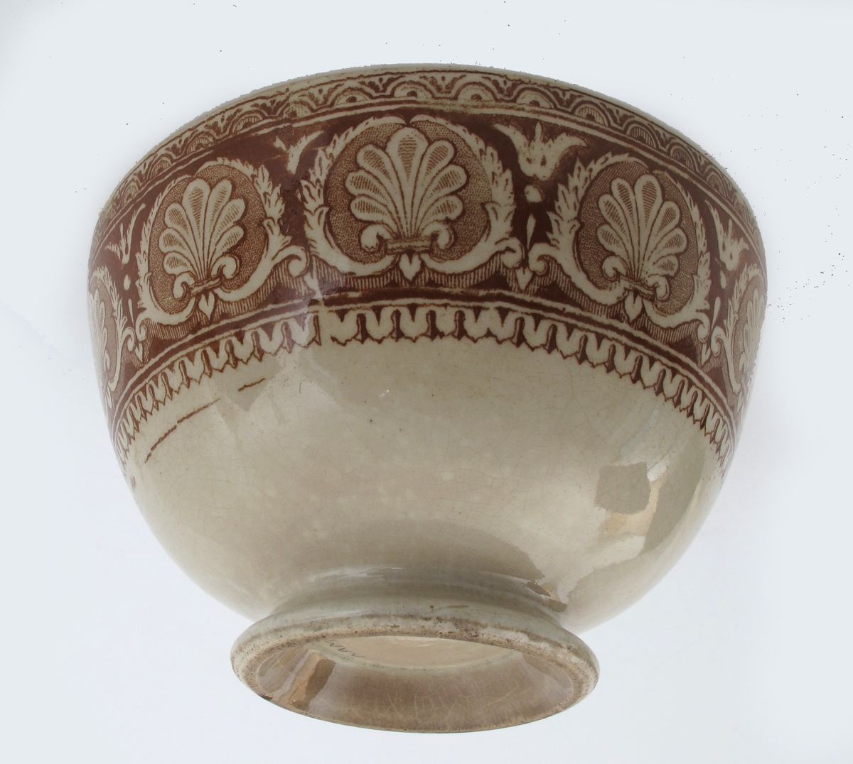 Bolle, stentøy, Buede sider, innsvunget fotring; trykt mønster i  brunt: Innv. og utv. bred ornamental bord m. skjell og "Garrya Eliptica" i bunnen lignende dekor, her er skjellene plassert i korsform i et rundt felt. Tilst. juli 1961: Krakellert.