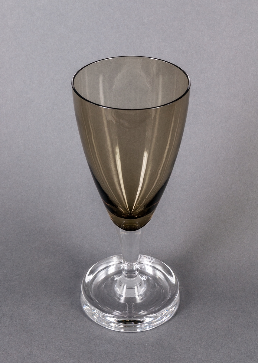 Vinglas, brungrönt, prov. Något konvex, trattformad kupa övergående i ofärgat ben på bred, konkav och ofärgad fot, bredast längst ut. Design Gunnar Cyrén för Orrefors Glasbruk.