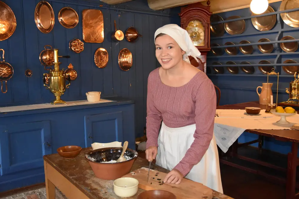 En tjenestejent står på et blått kjøkken og lager mat. 