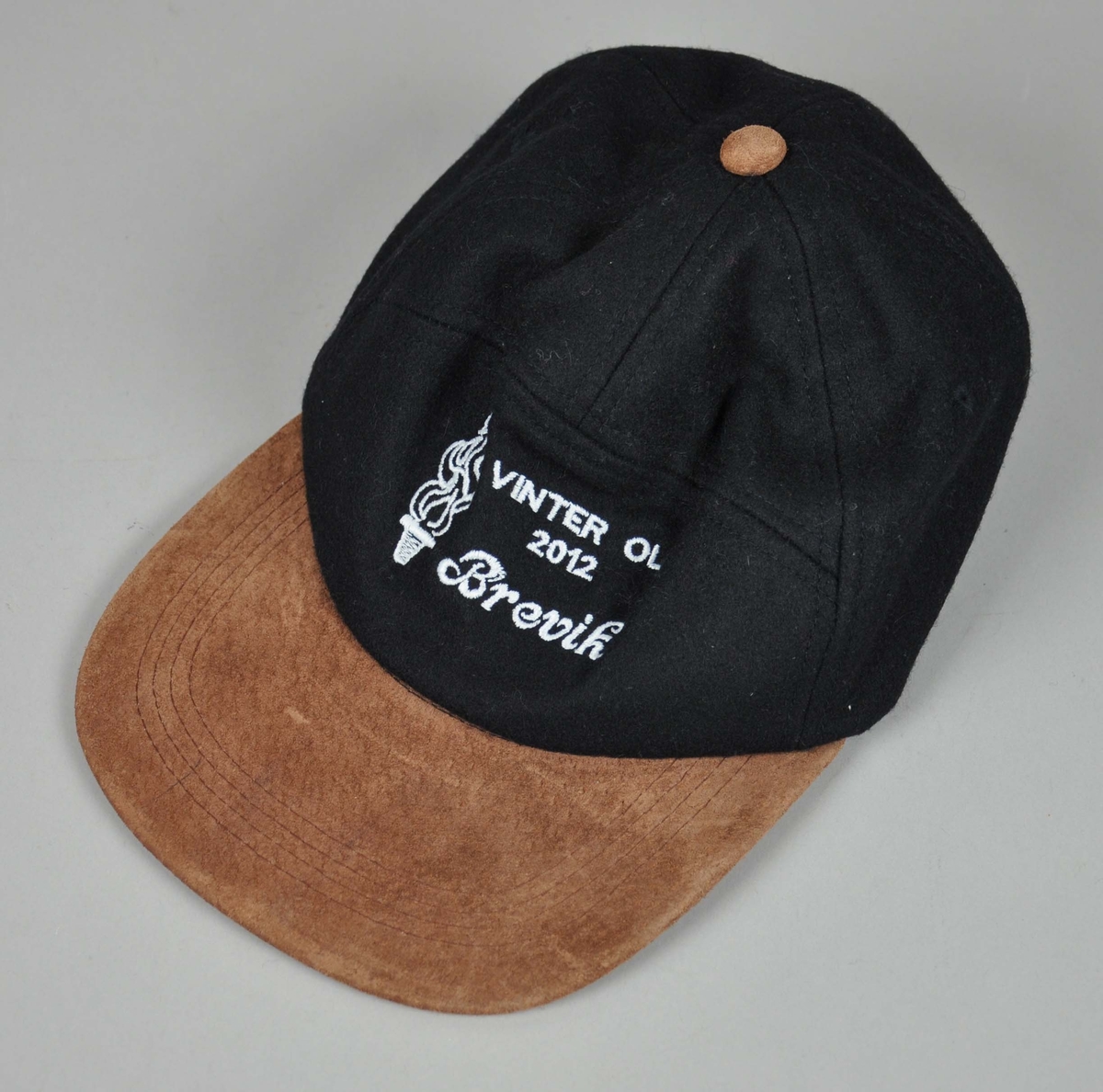 Mørkblå caps med brun skygge og brun skinn-knapp.Hvitt broderi med innskrift.