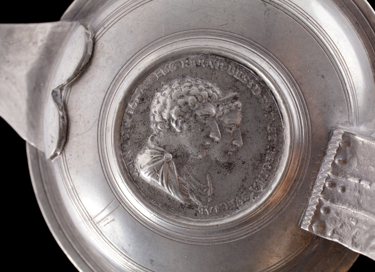 Stop i tenn. 
Cylindrisk, något avsmalnande modell med lock. Banddekor omväxlande med graverade blommor. På locket infälld hyllningsmedalj över Oscar I och hans gemål Josefina (nött och svårtydd text på latin). 
Stämplar på insidan i botten.