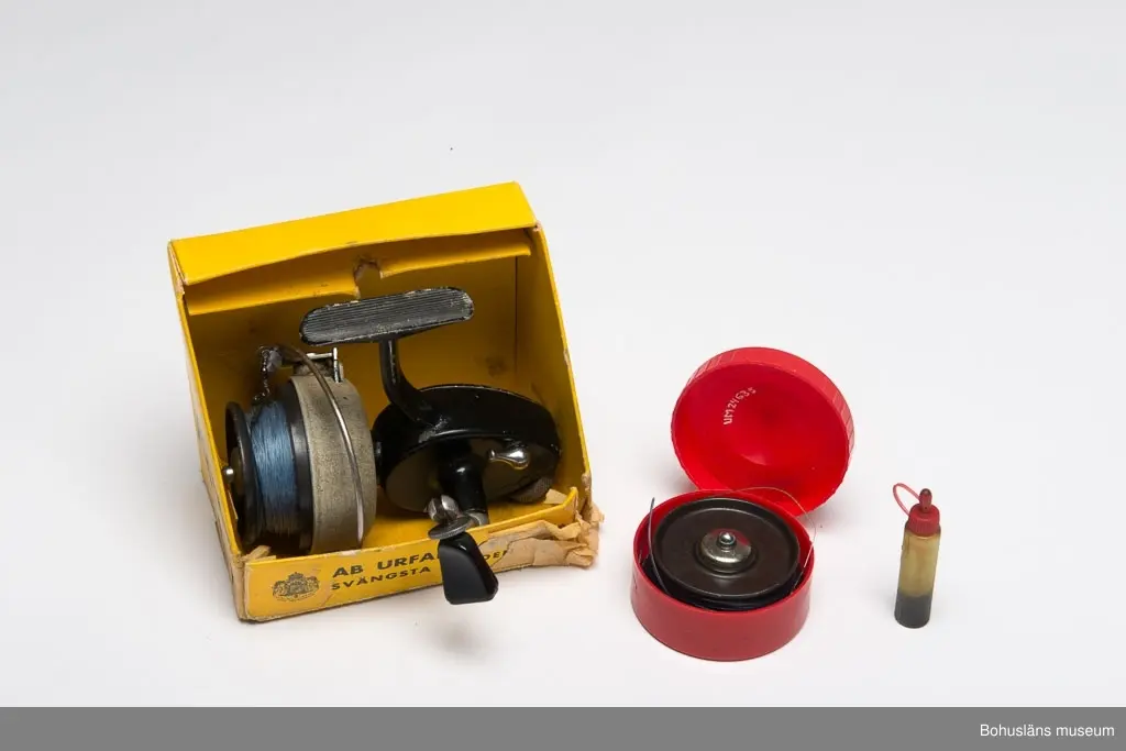 Svart haspelrulle med grått spolhus. Ledbart vevhandtag. Text på gavelplattan: "ABU 444 SVÄNGSTA SWEDEN". Blå lina av polyamidfiber En extra rulle i en röd cylindrisk ask av konstmaterial (H 2,5 Di 6,5 cm). Märkt "ABU SVÄNGSTA SWEDEN".
En behållare i konstmaterial med rullolja, den har rött lock samt samt text på kroppen "ABU SVÄNGSTA SWEDEN" (H 6,3 Di 1,2 cm) . En
broschyr "HANDBOK I HASPEL FISKE" (L 14,8 H 11,3 cm) med instruktioner om skötsel och användning av rullen. Samtliga föremål låg ursprungligen i en fyrkantig låda av papp (L 14 H 12 B 9 cm). Lådan är svart, gul och vit. Text bl a "ABU 444". Lådan är mycket lagad med tejp.
Tillhör fiskespö i fodral UM024251. Har även använts på UM023750.
*Tidigare sakord: Fiskerulle i originallåda.