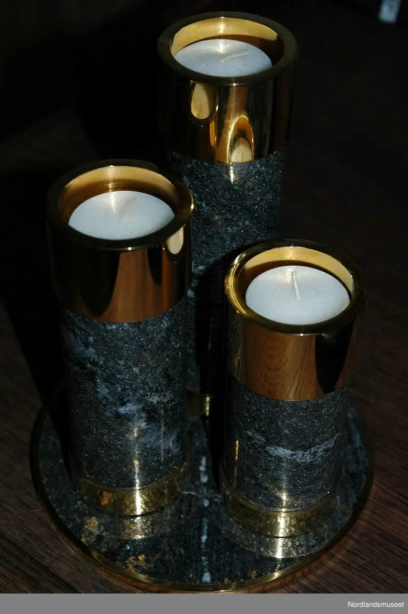 3 lysestaker med en brikke.
a: Lite lys som er laget av slipet malm og messing.
b: Mellomstort lys som er laget av slipet malm og messing.
c: Stort lys som er laget av slipet malm og messing.
d: Brikke som lysestakene står på.