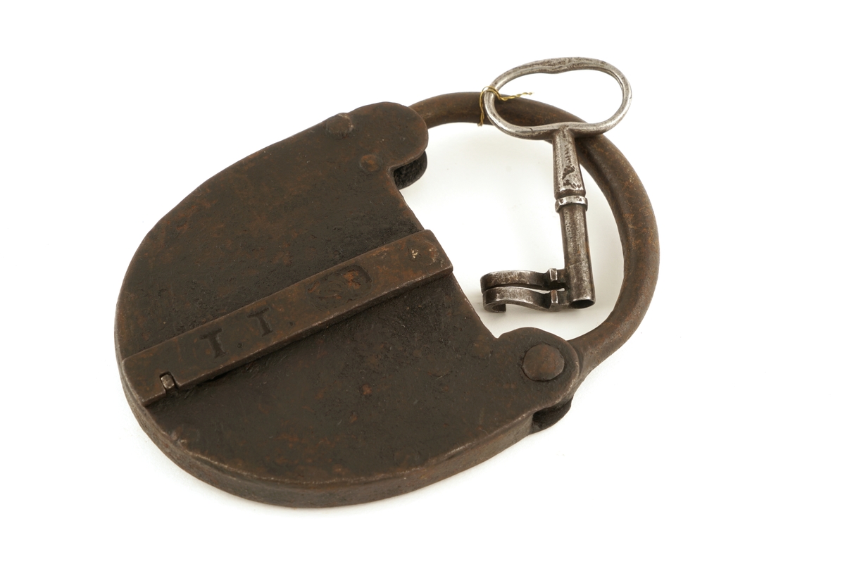 Hengelås av jern, oval med svingbart lokk over nøkkelhull.
Nøkkel av jern med skjegg formet somkroker. Gjennombrudt.