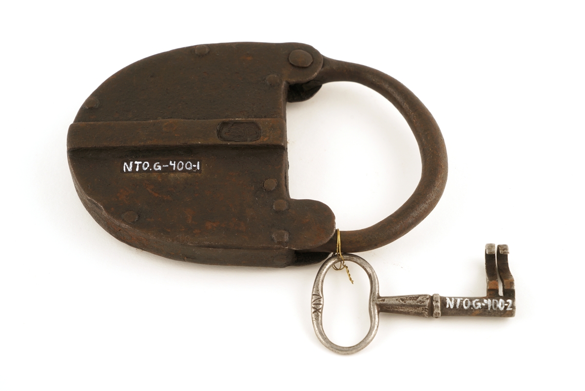 Hengelås av jern, oval med svingbart lokk over nøkkelhull.
Nøkkel av jern med skjegg formet somkroker. Gjennombrudt.