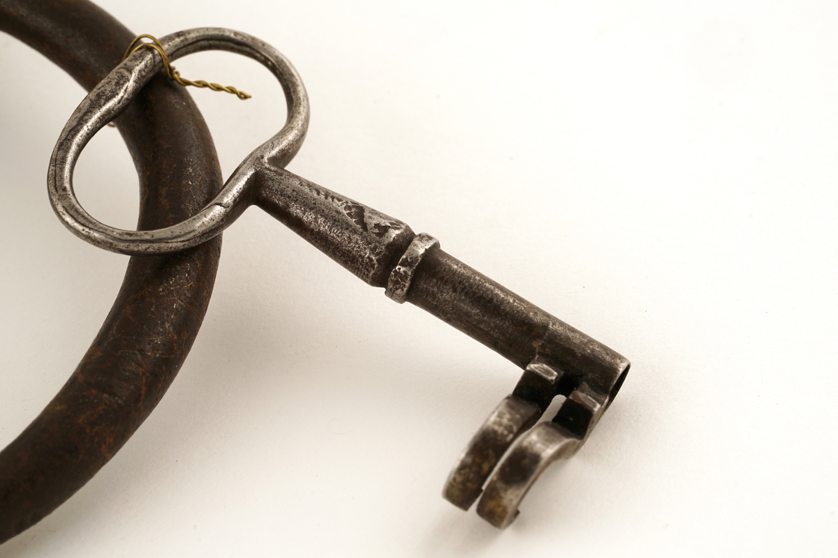 Hengelås av jern, oval med svingbart lokk over nøkkelhull.
Nøkkel av jern med skjegg formet somkroker. Gjennombrudt.