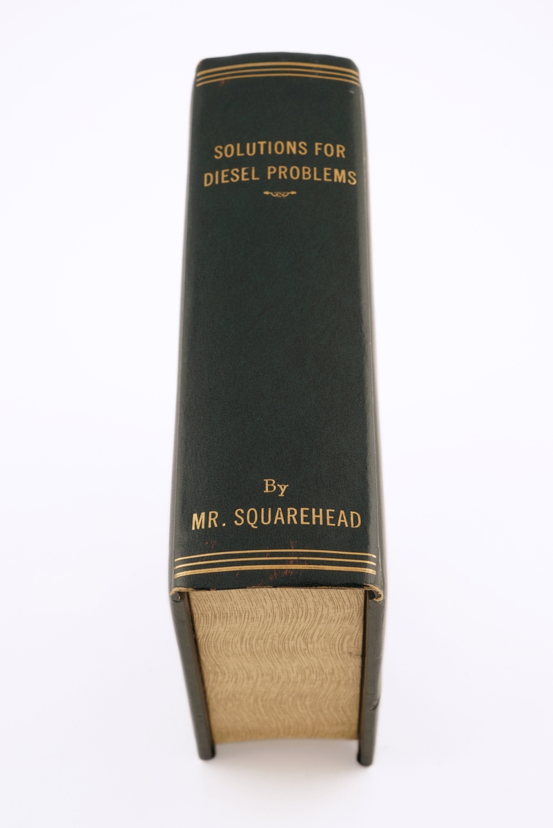 Bok i mørk grønt skinn. Det som skulle være boksider, er treverk. Dette er uthult for å romme sigaretter.