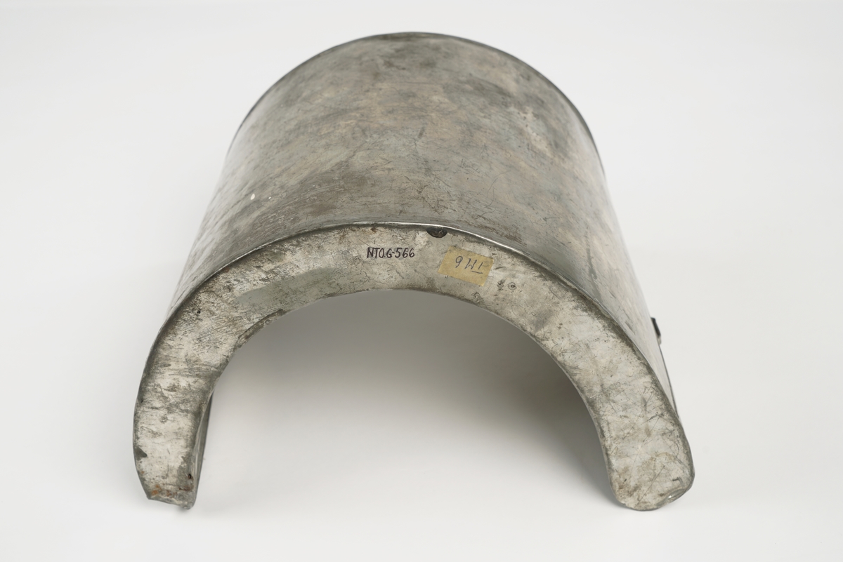 Halvrund blikktank for smugling av sprit eller brennevin. Tanken er utstyrt med hemper på hver sin side, og to steder på toppen for seler. Påfyllingsmulighet på toppen av tanken, med skru-kork.