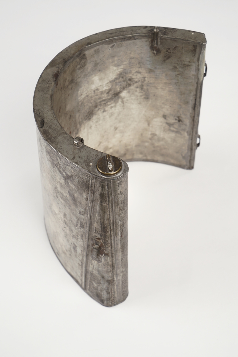 Halvrund blikktank for smugling av sprit eller brennevin. Tanken er utstyrt med hemper på hver sin side, og to steder på toppen for seler. Påfyllingsmulighet på toppen av tanken, med skru-kork.