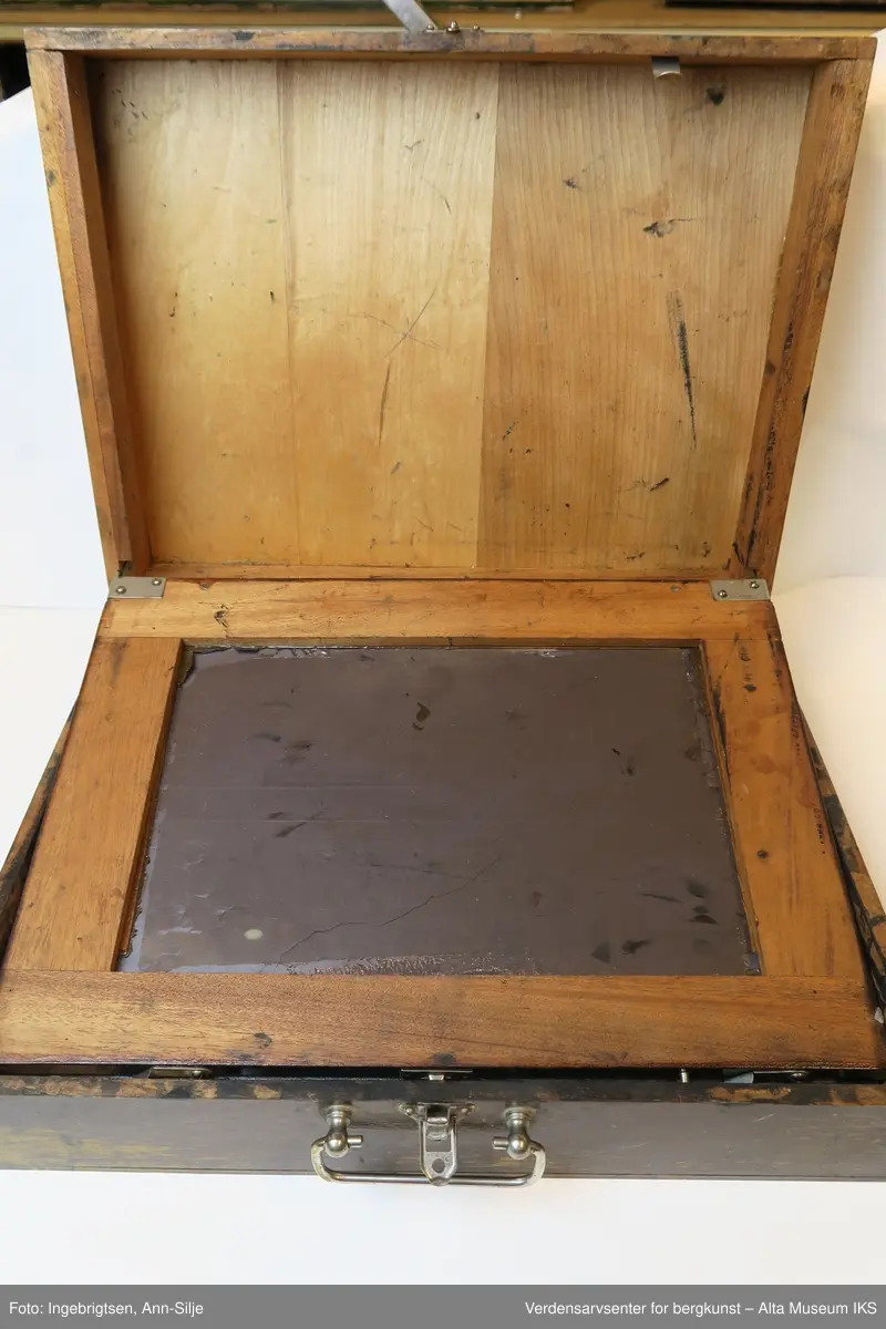Trekoffert med et lite metallhåndtak. Inn i kofferten er det sverterull, plater, et rutet ark og en sjablong med motiv av en blomst. Både platene og det inngraverte stykket har et lag av inntørket sverte.