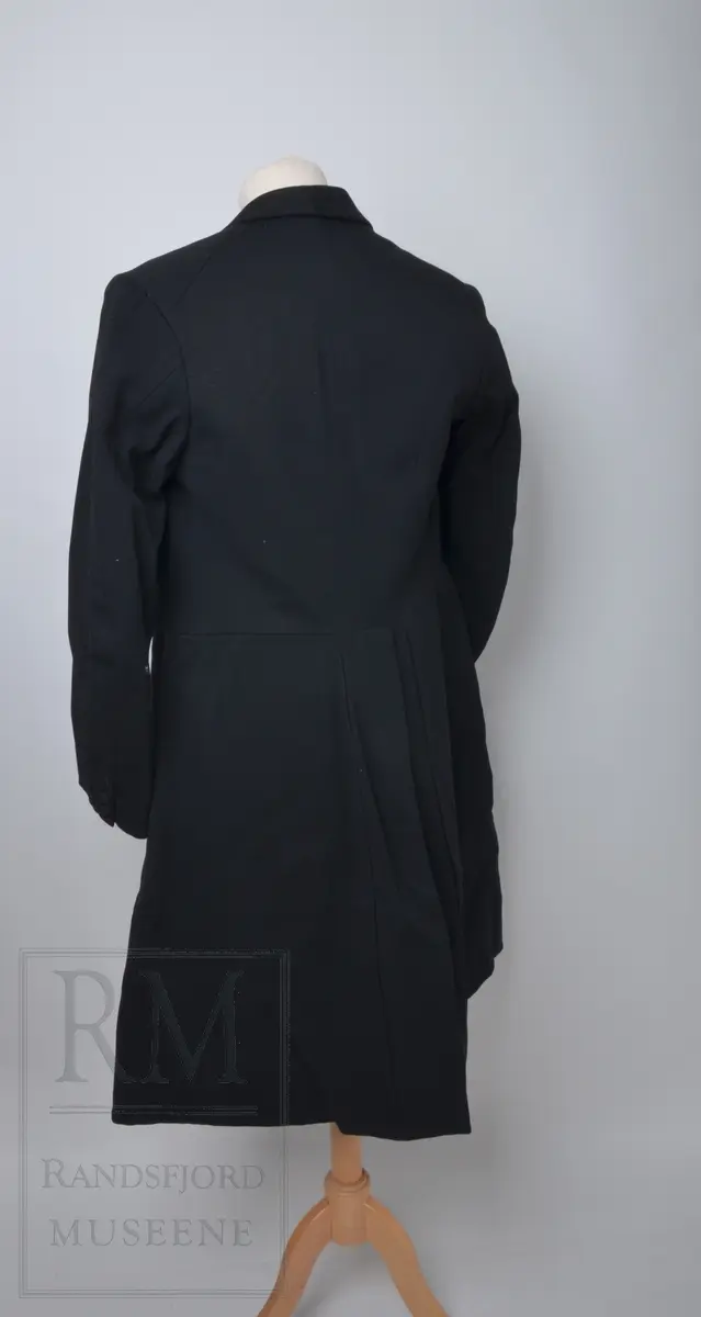 Tredelt dress med hvite hansker. Frakk av livkjoletype, kalt bonjour. Vesten har slag som er fôret med svart silkefôr på innsiden og har seks trekte knapper. Bunnfargen på fôret er hvit med brune og grå striper.