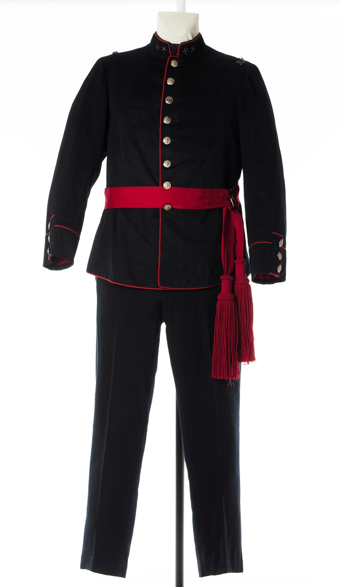 Enkeltspent jakke til uniform i mørk blå ull, med rød kanting og sølvnapper. Åtte knapper i fronten. Kraven er opprettstående og med to sølvstjerner på hver side. Skuldrene har tre påsydde hemper og metallkjede. Knappene er dekorert med norsk løve. Baksiden har splitt og tre par knapper. Rød kantdekor. Nederst på ermene er det tre smale bånd med knapp og røde kantbånd. Innvendig er jakken helforet med rødt stoff og lyst stripet stoff i ermene. Opphengshemper i ermene. Fronten er vattert. Innvendig hempe i midjen. To hekter i halsen for lukning av krave. Lomme i foret på hver side av splitten.

Bukse i mørk blå ull med to lommer foran og en bak. Gylf lukkes med metallhekte og fire plastknapper. Spenne øverst mot linning bak. Seks knapper i linning. En mangler. Striper av rødt stoff i sidene. Fôr i linning og litt nedenfor linning.

Belte i burgunder ull med store dusker i hver ende og messingspenne. Beltet festes rundt livet over jakken.