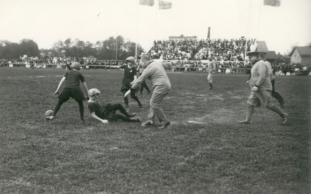 Motiv från firandet av Barnens Dag i Linköping 1922. Ögonblick från en lekfull fotbollsmatch mellan ett Oldboyslag och flickor från Linköpings gymnastikförening. I det manliga laget deltog grosshandlare Arthur Magnusson, åkaren F. G. Edman, stadsbudet L. E. Sandberg, föreståndaren Hj. Örtengren, författaren Nils Larsa Waange, direktörerna Salomon Löwentahl, Ernst Clason, Anton Klingblom och kamrer C. L. Sabelström samt grosshandlare Edvald Björkman. I gymnastikföreningens lag ingick målvakten Maja Broström, backarna Elna och Siri Jonsson, halvbackarna Anna Sik, Stina Rosén och Edit Dahlgren, yttrarna Toto Johansson och Märta Persson, innrarna Stina Hansson och Siri Idén samt som centerforward Greta Seger. Som domare agerade förtjänstfullt Åttmar Stenborg, som ÖC beskrev vara "tränad i grenen och säker i uppfattningen". Matchen spelades på Folkungavallen och slutat med seger för flicklaget, efter att den artige domaren tilldömt laget en mycket tveksam straff.