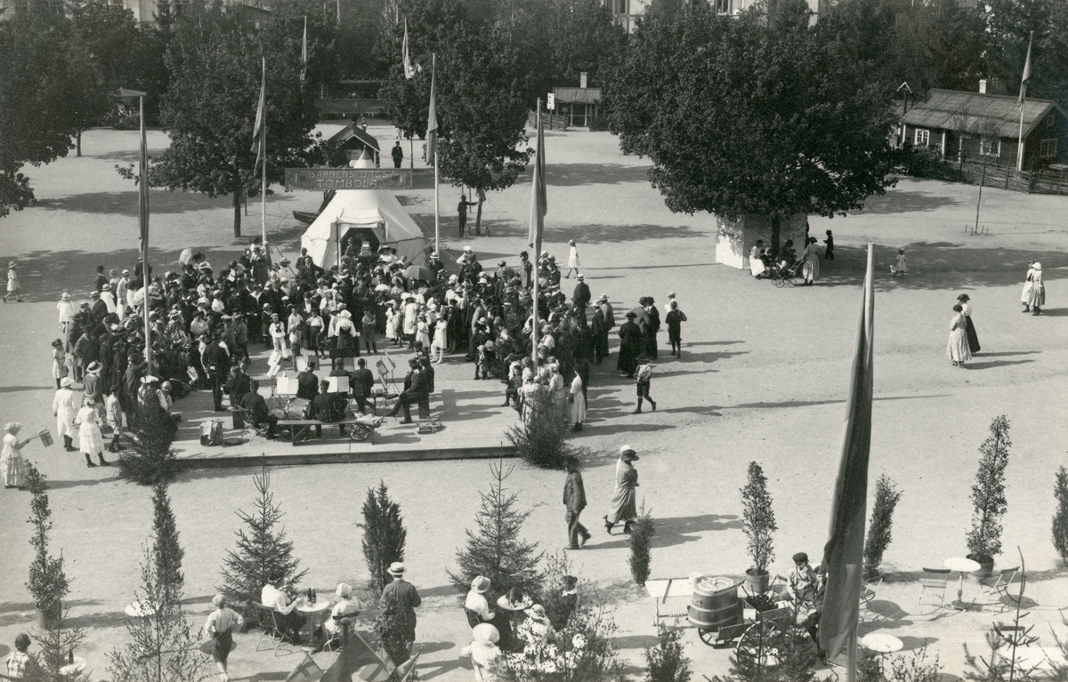 Motiv från firandet av Barnens dag i Linköping 1922. Vy över arrangemangets festplats invid Linnéskolan. Orkestern är Andra livgrenadjärregementets musikkår.