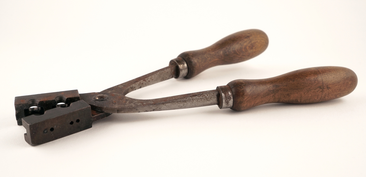 Plombestøpetang av jern m/ treskaft.
Utstyrt med fire hull. De to på oversiden var for flytende bly. De to på siden var til bruk for en spesiell
"gaffel", som skulle lage hull i plombene for forseglingstråden.