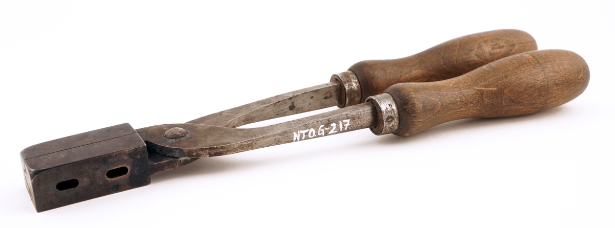 Plombestøpetang av jern m/ treskaft.
Utstyrt med fire hull. De to på oversiden var for flytende bly. De to på siden var til bruk for en spesiell
"gaffel", som skulle lage hull i plombene for forseglingstråden.