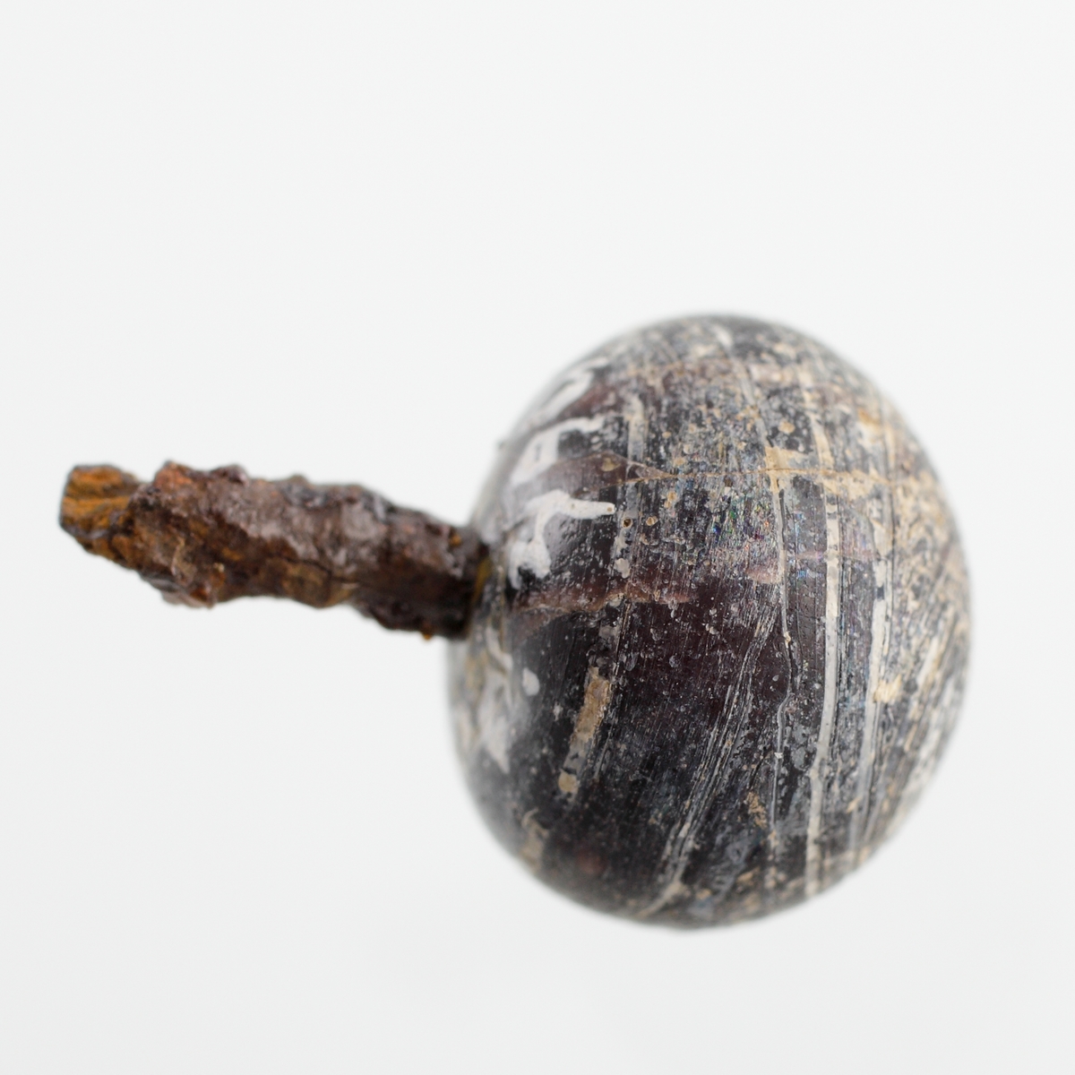 Klotformad knapp av svart, opak glasfluss med vit marmorering. Matt glasyta. En stump av järnöglan sitter kvar. Tidigare tolkad som en recent nål. Se Referenser/Digitala objekt för liknande knapp i 1500-1600-talskontext.