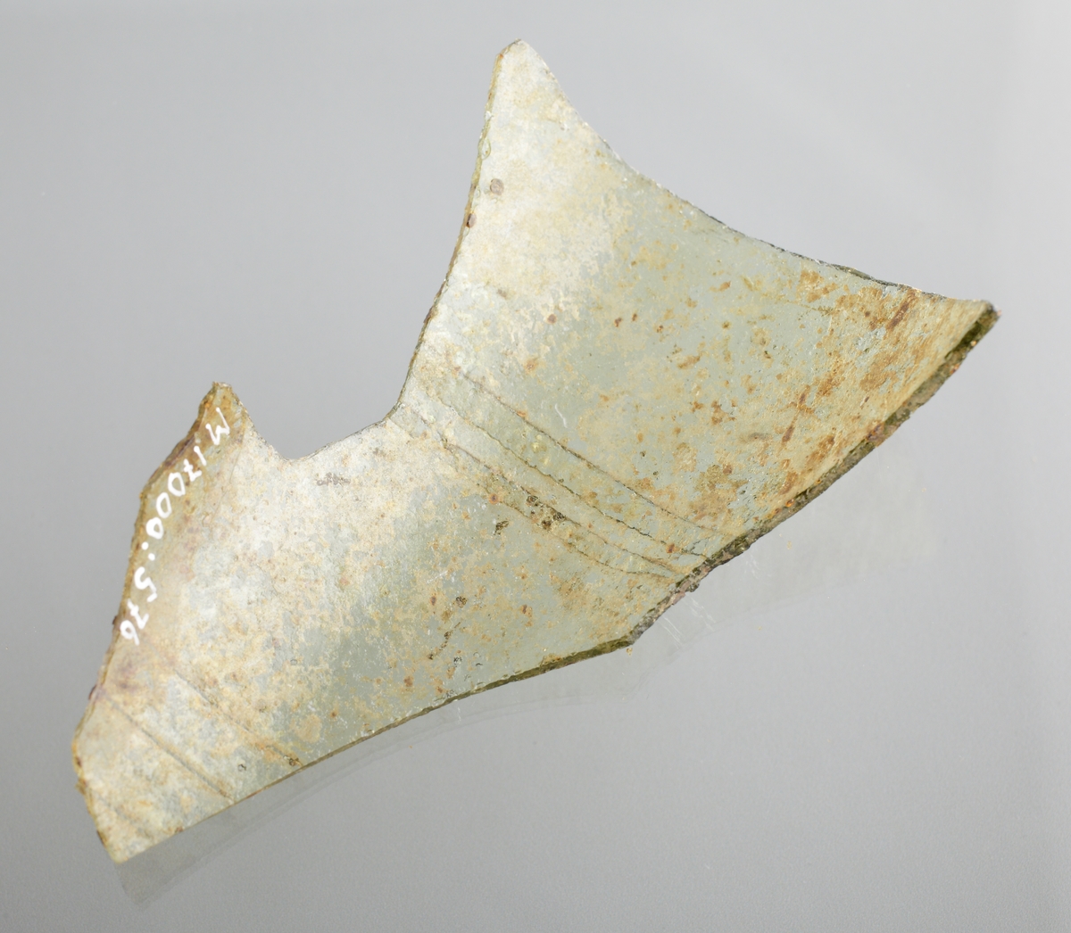 Del av buken på ett ofärgat, kägelformat, optikblåst passglas som är ornerat med fem pålagda parallella trådar. De två övre trådarna är strierade. Fragmetet har glaspest.