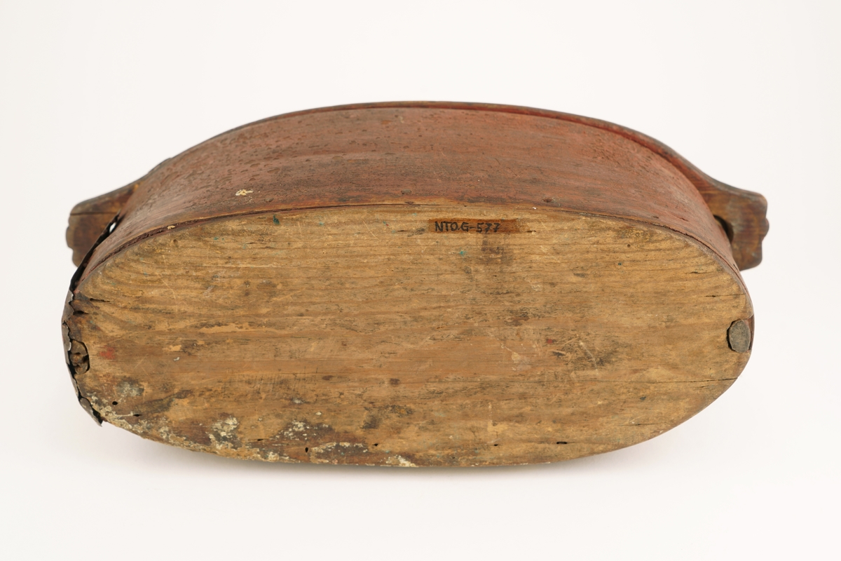 Nistelaup av rødmalt tre. Oval med svingbart lokk, festet i den ene enden med en trenagle. Hank og lås på lokket.