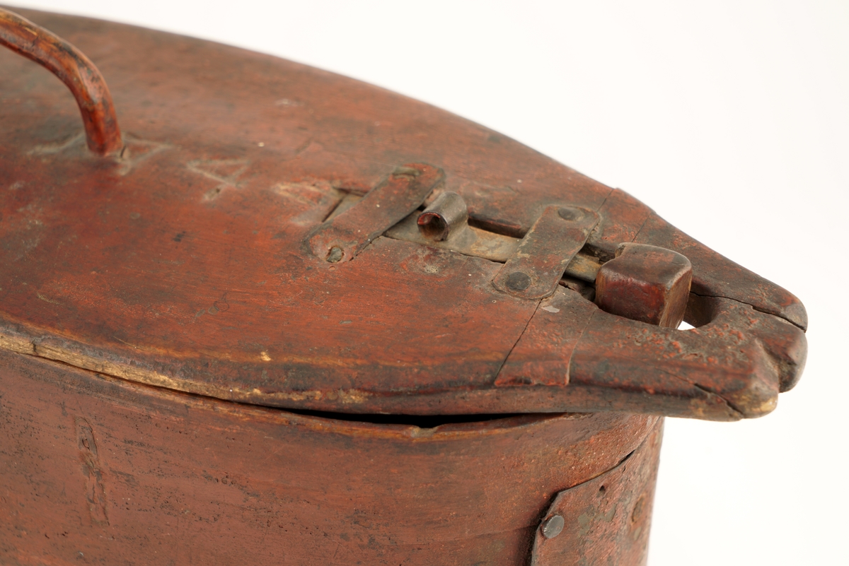 Nistelaup av rødmalt tre. Oval med svingbart lokk, festet i den ene enden med en trenagle. Hank og lås på lokket.