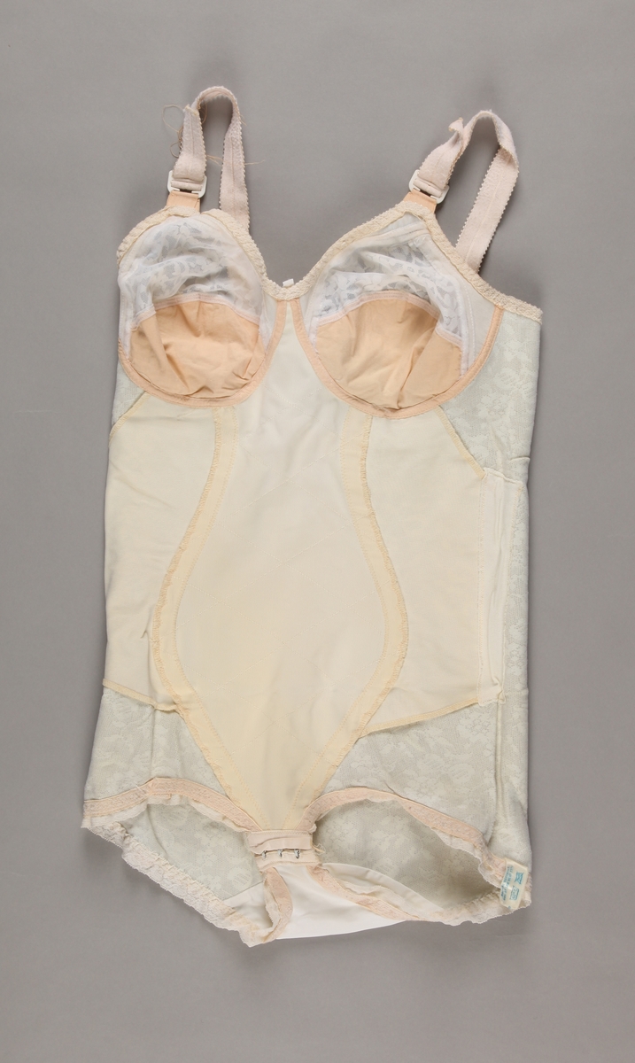 Korselett i blondevevd stoff med sateng panel. BH-del i blonde og hudfarga bomull (?). Lukking med 3 hekte under skrittet. Ingen stropper. Storleik 38C.