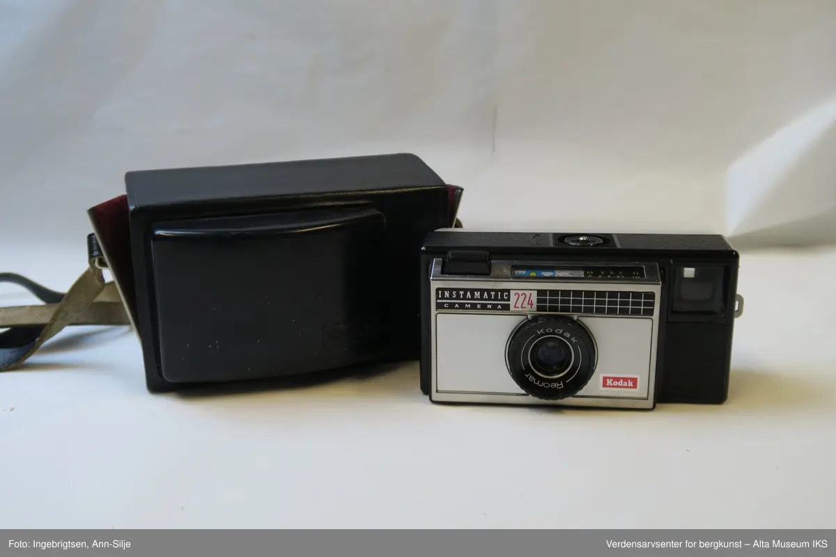 Fotoapparat i rektangulær form. Den er festet i et læretui med rødt tøystoff på innsiden. Inn i apparatet er det en filmrull av merket Fuji. På toppen av apparatet, ved siden av utløseren, er det symboler av vær og landskap.
