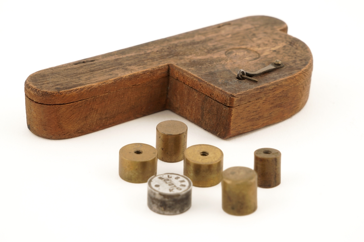 1 tre - eske inneholdende 6 stk. lodd. På oversiden av esken finnes et utydelig merke.
Esken er P - formet.