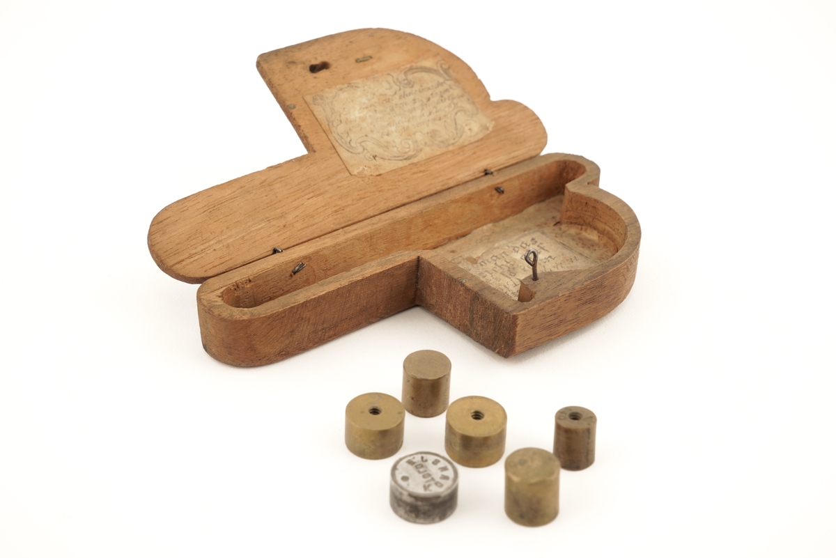 1 tre - eske inneholdende 6 stk. lodd. På oversiden av esken finnes et utydelig merke.
Esken er P - formet.