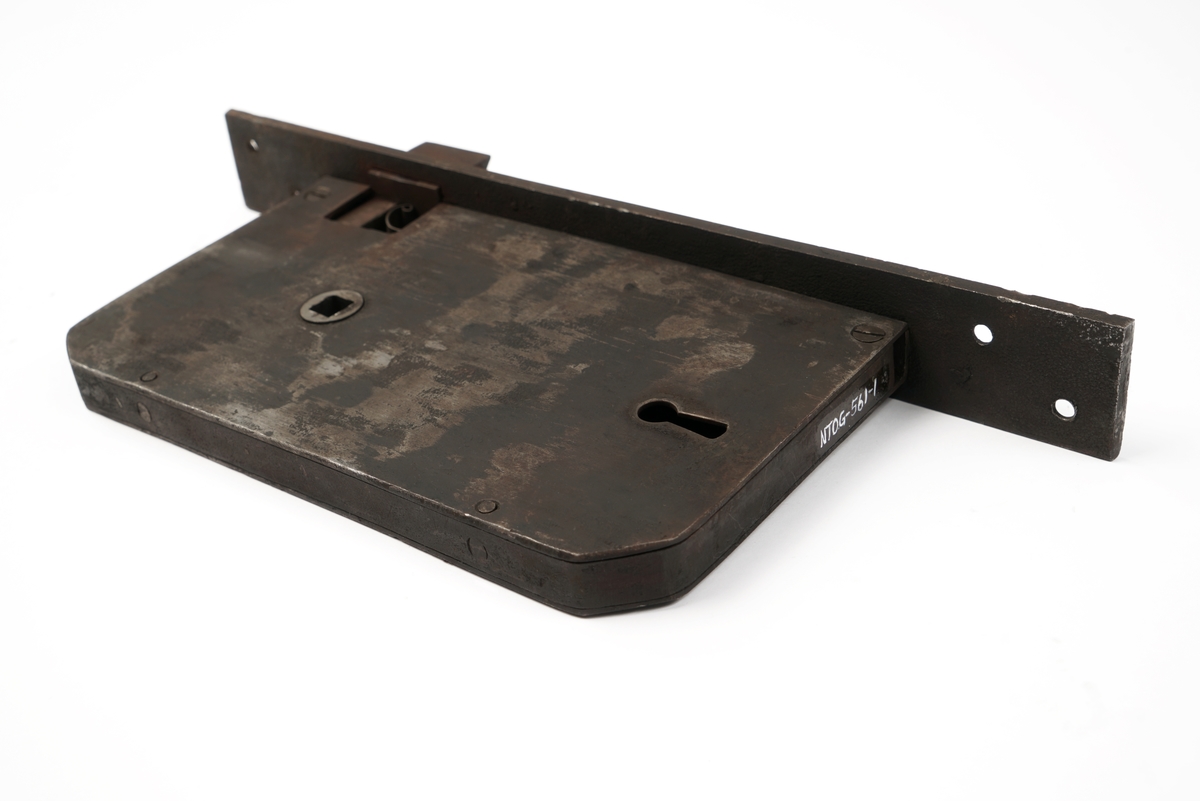 Dørlås for innmontering i dør av jern. Det medfølger tre monteringsbraketter, som selve låsen har vært montert på. Låskassen er rektangulær, med avrundede hjørner på den ene siden, og et større, flatt jern på den motsatte siden.Nøkkel følger med