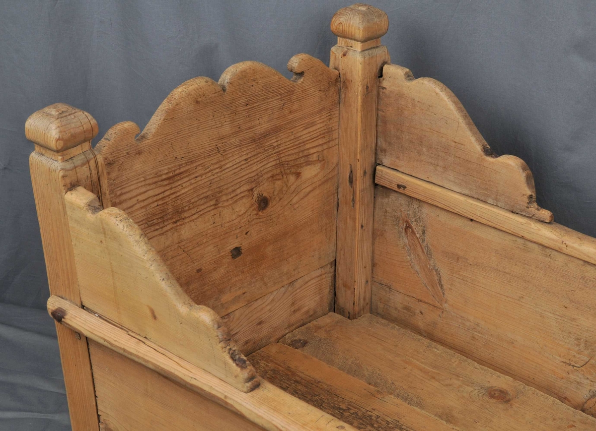 Vogge med nedslitne meiar. Botn er sett saman av 3 bord som ligg lause. Toppen av endeveggane, samt sidekantane er utskorne i bogeformer. Stolpane er firkanta med enkle, utskorne kuler på toppen. Vogga er noko slarkete og slitt.