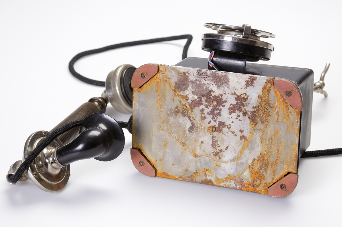 Telefon, bordsmodell. 
Rektangulär, svart bakelitmodell med detaljer av nickel. Telefonlur med svart tygsladd.