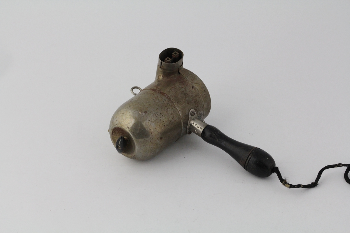 Sylindrisk del med stanghåndtak på undersiden. Utskåret rosettmønster i front, vifte inni. Side v/front: utstikker. Bakside buer inn mot bryter. Ledning går ut fra nedersiden av håndtaket, kontakt i enden. Metallring for oppheng på oversiden av sylinder.