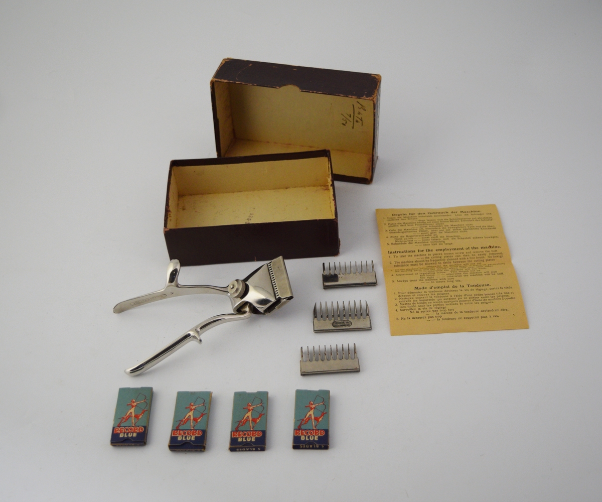 Eske inneholdende saks, tre ekstra utskiftbare deler til saksen, en fjær, en metallplate, fire pakker med flere barberblad og en lapp med instruksjoner for bruk og vedlikehold på flere språk, deriblant engelsk.