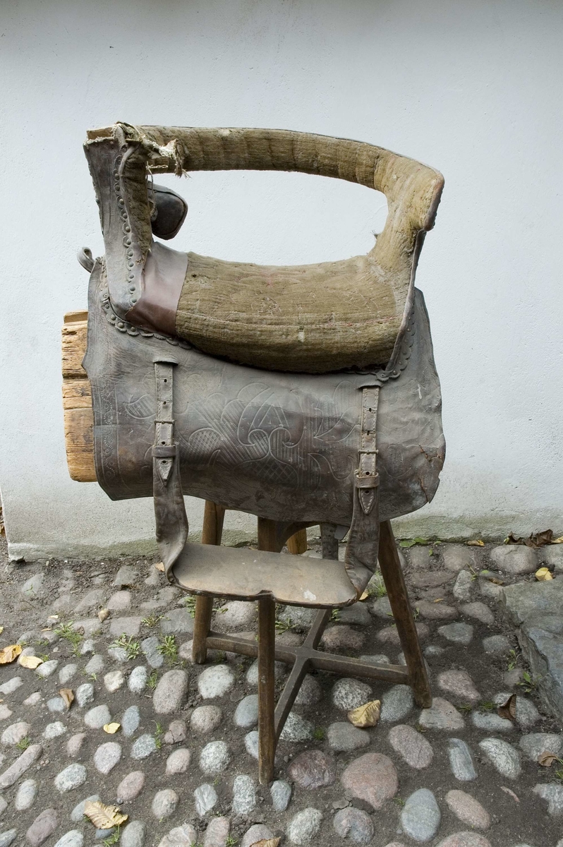 Brudsadel, handgjord. Modell där den ridande färdas sidledes, med fötterna på samma sida på ett fotstöd. Försedd med ryggstöd.
Stomme av trä. Sitsen, sido- och ryggstöden stoppade och klädda med grön ylleplysch, nersydd i mönster med röd tråd, troligen av lin. På utsidan är stöden klädda med brunt skinn, plåt och nitar. Både plåt och skinn har genombrutna partier, med underliggande rött kläde. Märkningen GTDR (osäker) samt 1809 är utskuret i plåt med rött kläde under. Detta är placerat på bakre sidostödet. På båda sidorna hänger stycken av läder med rundade hörn, med präglat mönster som liknar en blomsteruppsättning av barocktyp. Fotstödet hänger på vänster sida, i justerbara remmar av läder med söljor av metall. Trästommen är också stoppad ned mot hästryggen, och klädd med säckväv av jute. Det finns också remmar för fastsättning av sadeln, men de är korta och måste skarvas. Allt trä klätt med målad säckväv.