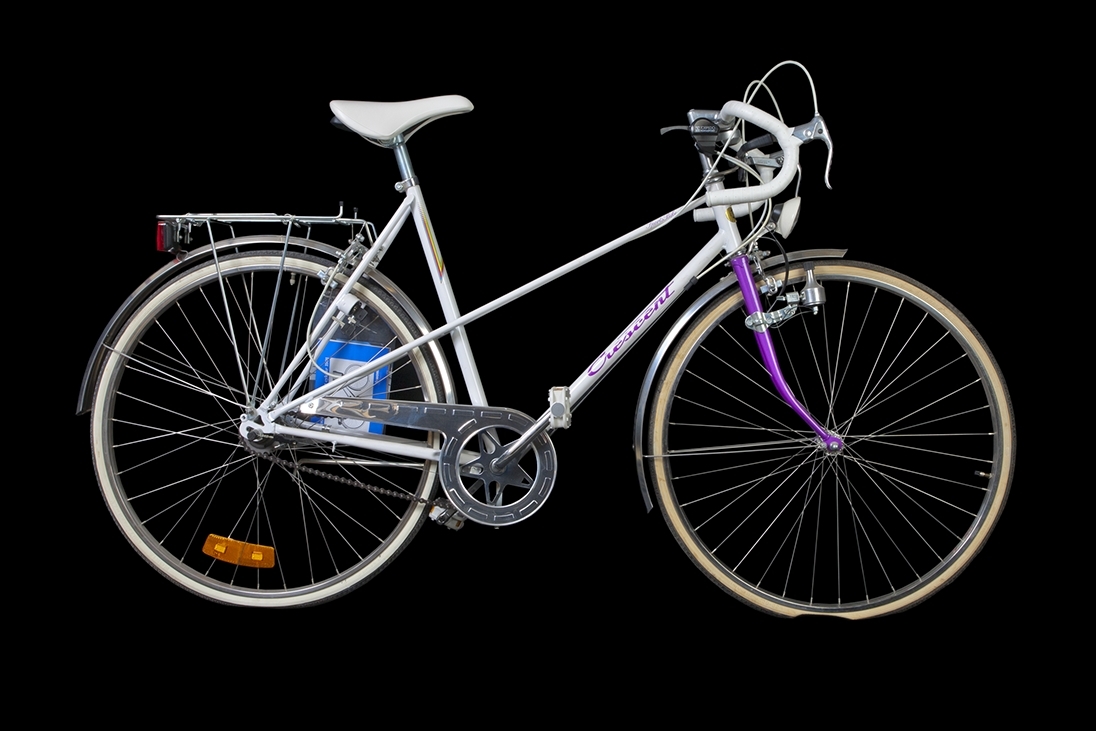a) Lila/vit 5-växlad Crescentcykel. Bockstyre med vit lindning. Två handbromsar samt fotbroms. Vit sadel märkt "Iscaselle". Reflex på bakhjul, ej fram. Märkning: Crescent. Sports Bike. Crescentemblem fram. 1990-tal. b) Instruktionsbok. Monark och Crescentcyklar 1991.